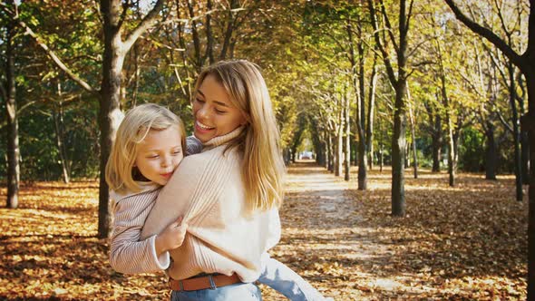 Young Mom is Smiling Holding Little Daughter in Her Arms and Circling Around During Their Walk in