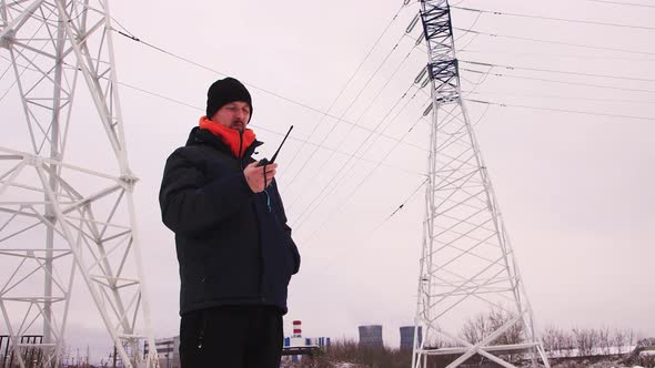 A Man Stands Against a Gray Sky and Communicates on a Walkietalkie