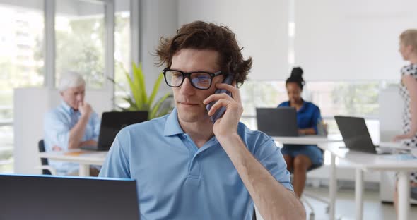 Portrait of Young Entrepreneur in Casual Office Making Phone Call While Working with Laptop