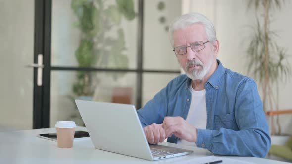 Senior Old Man Looking at Camera While Using Laptop in Office