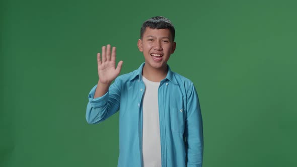 The happy young Asian man waving hand while standing on green screen in the studio