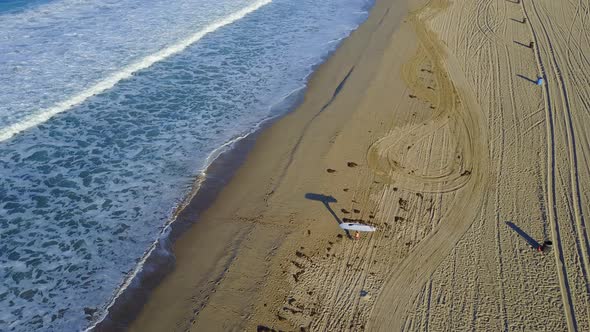 Aerial drone uav view of a surfer walking with his sup surfboard.