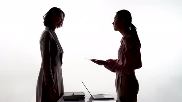 Silhouettes of two businesswomen while signing contracts and they are shaking hands for success 