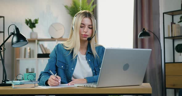 Female Student in Headphones Doing Notes Into Paper During Online Video Meeting
