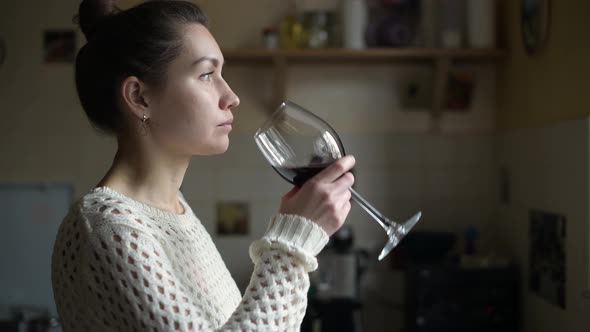 girl comes with a glass of wine to the table in the kitchen, and drinks