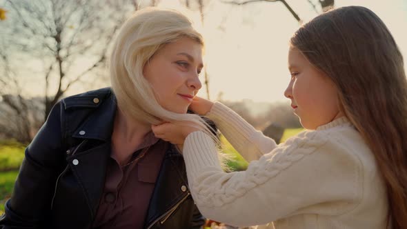 Mother and daughter sitting at autumn park outdoors. Child girl hug woman face. Love in family