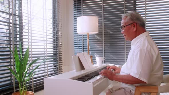 An elderly Asian man practicing playing the piano in the living room