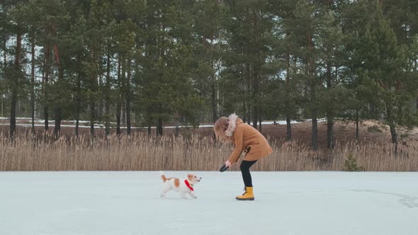 A girl in a coat and yellow boots plays in the winter on the ice of the lake with a dog