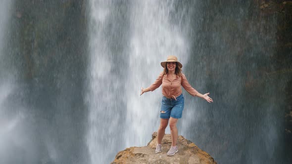 A Young Woman Traveler Admires a Waterfall and a Huge Stream of Water in Delight