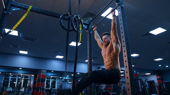 Bodybuilder exercising on horizontal bar. Shirtless man pulling up on horizontal bar in gym