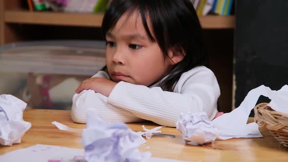 Little girl cutting paper with scissors alone, playing with sharp cutting objects.