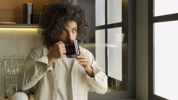 Muslim Man Enjoys Hot Tea Standing Near Window in Kitchen