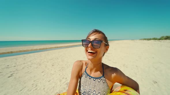 Smiling Girl on Sunny Ocean Beach Looking at Camera Through Yellow Inflattable Ring with Funny Face