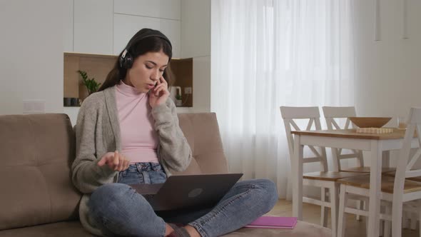 Young 20s Enterpreneur Woman Making a Sale on a Call Using Headphones and Laptop on a Couch in