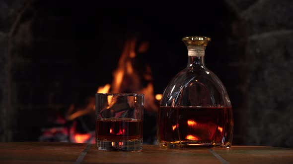 Bottle and Glass with Whiskey or Cognac on the Background of Fire in the Fireplace