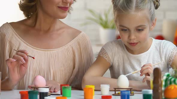 Mother Watching Daughter Painting Easter Egg for First Time, Family Traditions