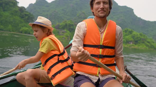 A Young Man and His Son on a Boat Rowing Together on a River Trip Among Spectacular Limestone Rocks