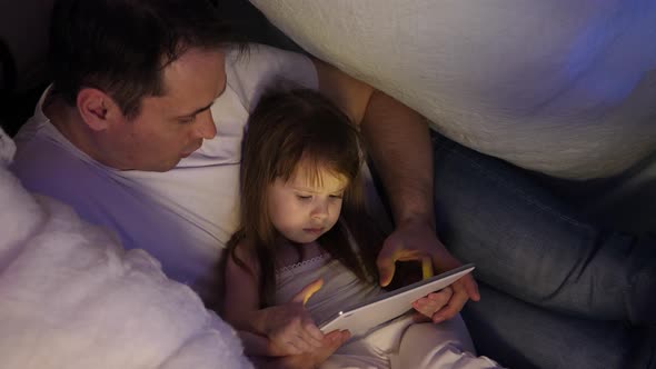 Concept of a Family Christmas. Child and Dad on Christmas Evening Play on Tablet, in Children's Room