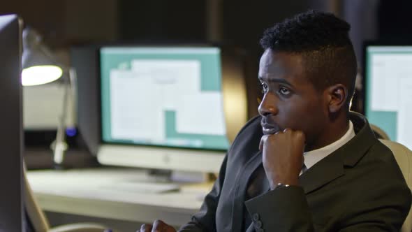 African Businessman Surfing the Net on Computer in Dark Office