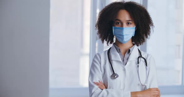 Young Woman Doctor African Lady in White Gown, Wear Face Mask Crossing Arms Standing in Clinic Alone