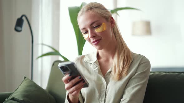 Serious blond woman with sticking patches to eyes texting by phone