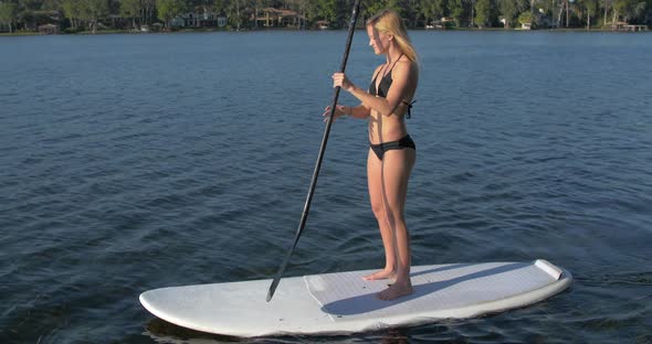 A young woman sup stand-up paddleboarding on a lake.