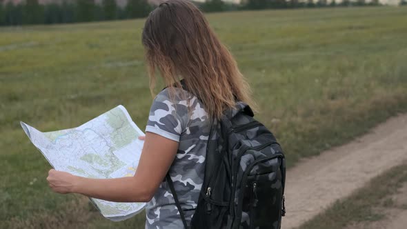 Beautiful Woman Tourist with a Backpack and with a Map in Hand Stands on a Background of Mountains