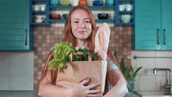 Portrait woman with bag of food in hands in kitchen looks at camera, smiling