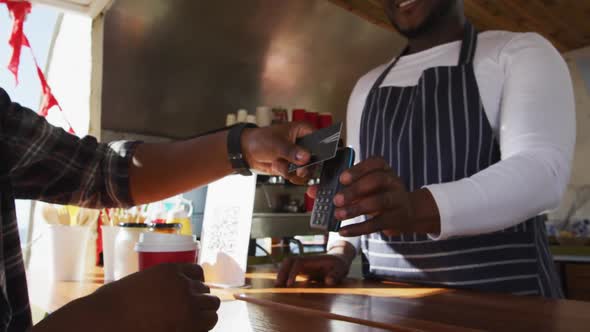 Midsection of african american man paying male owner for coffee by credit card at food truck