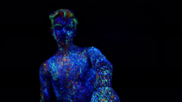 Young Man Painted with Fluorescent Paints Makes Movements with Hands Front View