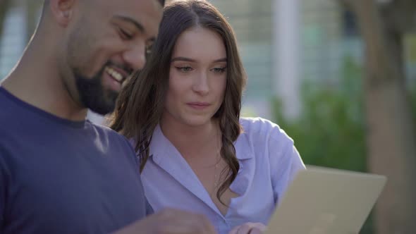 Young Man and Pretty Woman in Park Looking at Laptop, Discussing 