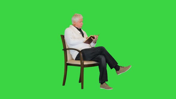 Senior Man Studying a Book Sitting in a Chair on a Green Screen Chroma Key