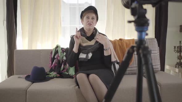Senior Female Blogger Sitting on the Couch in Elegant Hat and Scarf and Recording Video for Internet