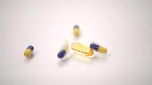 Slow Motion Macro of Blue and Yellow Pills Dropped onto One Yellow Pill on White Background