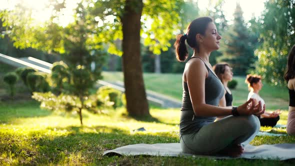 Woman Sitting on Yoga Mat in Lotus Pose and Meditating in a Park at Sunrise