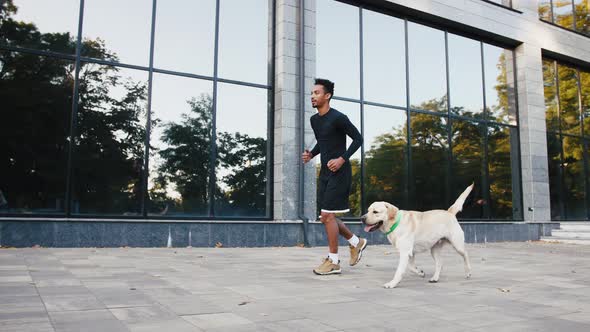 Young Black Man Running with His White Labrador Dog in Buseness City Center During Beautiful Fall