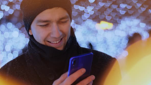 The Guy Uses a Smartphone Among the Christmas Lights