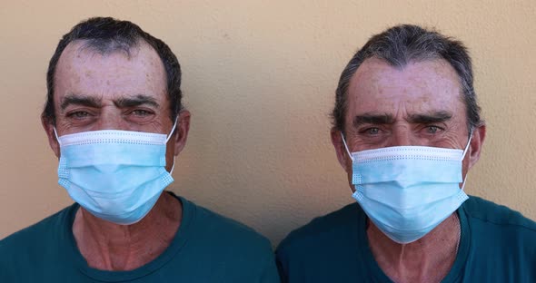 Senior twin men looking and smiling while wearing safety face masks for coronavirus outbreak