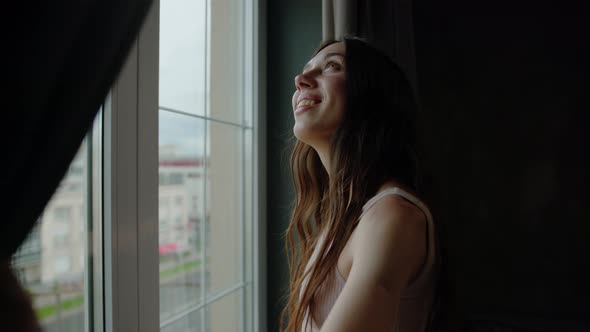 A Young Woman Opens the Curtains in the Apartment and Enjoys the Morning Sun