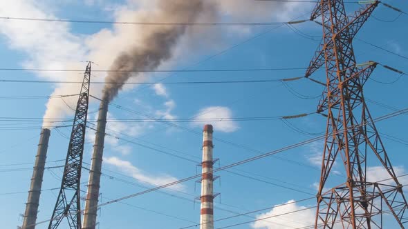 High Voltage Electric Pylons Against Coal Power Plant High Pipes with Black Smoke Moving Upwards