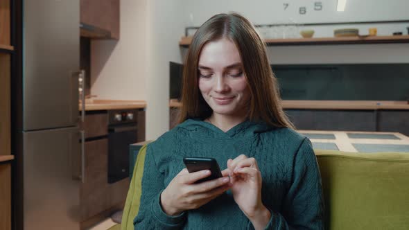 Happy Young Woman Holding Smartphone Looking at Screen Enjoying Using Mobile Apps Having Fun Playing