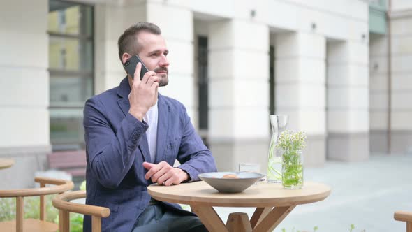 Man Talking on Smartphone Sitting in Outdoor Cafe Side Pose