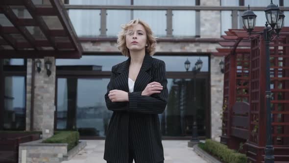 Stylish Thoughtful Model in Black Suit Stands in Poses with Crossed Hands