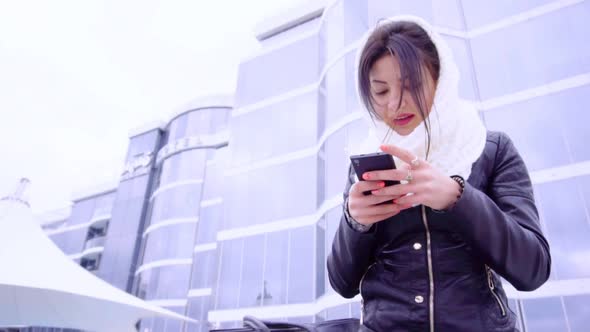 Young Brunette Woman Sits Outside with Her Phone