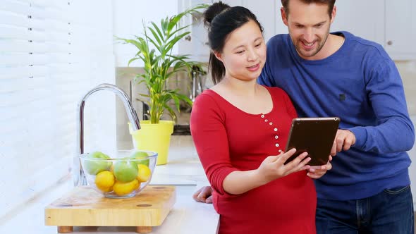 Pregnant couple using digital tablet in kitchen at home 4k