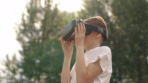 Happy Boy in Virtual Reality Glasses Plays Video Games Outdoors