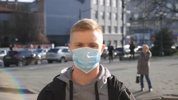 Portrait of Young Man with Medical Face Mask Stands at City Street. Happy Guy Take Off Protective