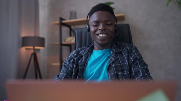 Joyful Young African American Man in Earphones Waving at Laptop Web Camera Smiling and Talking in