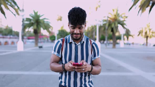 Young Trendy Hispanic American Man Using Mobile Phone While Walking Outdoor