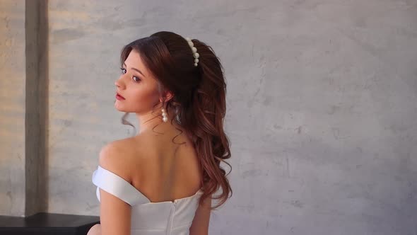 A Girl in a White Dress Poses for the Photographer with Her Back Turned